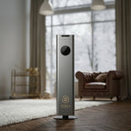 Otura Essence Modern air purifier in a living room setting with large windows and a brown leather sofa.